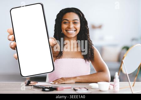 Woman Shows Smartphone While Smiling in Modern Room With Beauty Products on Table Stock Photo