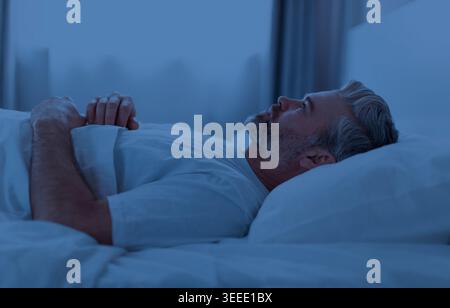 Sleepless middle aged man lying in bed at night Stock Photo