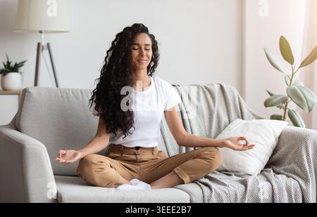 Peaceful brunette lady sitting on couch, meditating Stock Photo