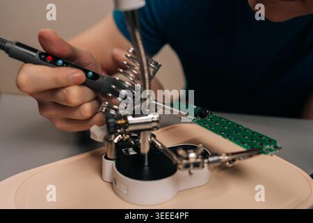 Technician using a soldering iron and magnifier to repair an electronic circuit board, focusing on precision engineering, electronics maintenance, and Stock Photo