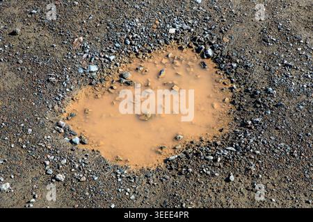 A closeup view of a muddy pothole in a dirt road, The pothole has gravel in it. Bright sunny day. Stock Photo