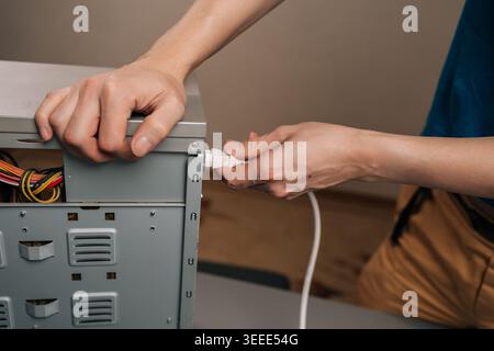 Person connecting power cable to computer desktop system unit, installing power supply for technology hardware and electronic device setup, preparing Stock Photo