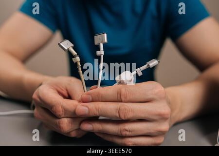 Hands holding several worn, frayed laptop charger and usb cables with exposed wires and broken connectors, illustrating durability issues, repair need Stock Photo