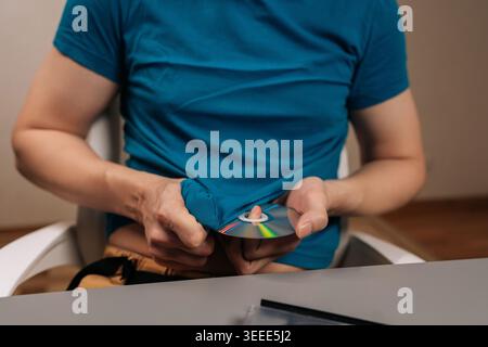 Closeup cropped shot of person cleaning a data disk with a t shirt before using an external optical drive connected to a modern laptop for important d Stock Photo