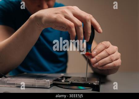 Technician repairing external optical disc drive, performing maintenance on the hardware, disassembling the casing of the cd dvd reader writer on a ta Stock Photo