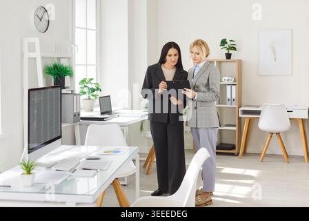 Two businesswomen discussing project in office while reviewing financial data on digital tablet. Stock Photo