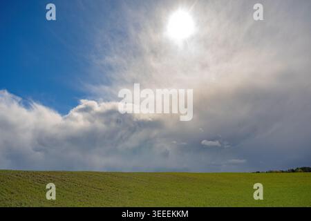 Dramatic spring sky above a green field with bright sunlight breaking through dense storm clouds, creating a striking contrast of light and atmosphere Stock Photo