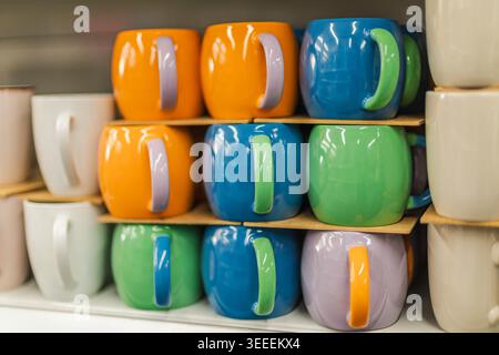 Colorful ceramic coffee mugs displayed on shelf in household goods store Stock Photo
