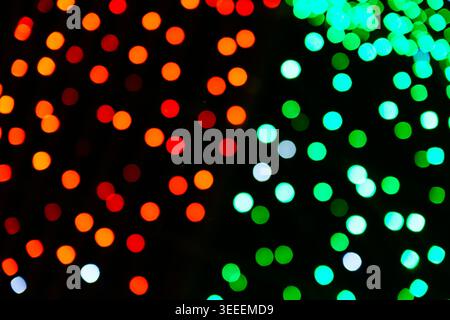 Out of focus illumination creating colorful bokeh lights. Abstract background pattern of glowing red and green circular blurs on black texture. Stock Photo