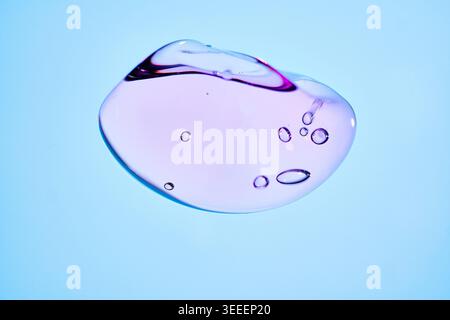 Single transparent gel drop with purple tint and air bubbles on soft blue background, macro cosmetic texture for skincare, serum and hydration design. Stock Photo