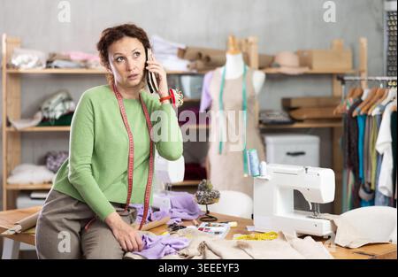 Female tailor talking on phone in sewing workshop Stock Photo
