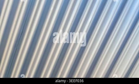 White corrugated metal sheet featuring parallel diagonal lines and play of light and shadow. Ideal as neutral, minimalist background for industrial or Stock Photo