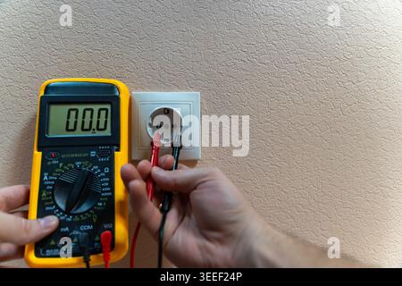 Hand Measuring Socket Voltage With Multimeter, Technician Diagnosing Live Circuit At Wall Outlet, Probe Tips Contacting Terminals, Digital Display Stock Photo