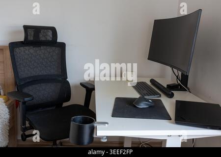 Modern home office workspace with ergonomic mesh chair, curved ultrawide monitor, wireless keyboard and mouse on clean white desk. Remote work Stock Photo