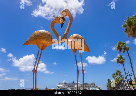 Iconic twin flamingo sculptures forming a heart shape at the Oranjestad waterfront, Aruba, with a cruise ship, palm trees and blue sky in the backgrou Stock Photo