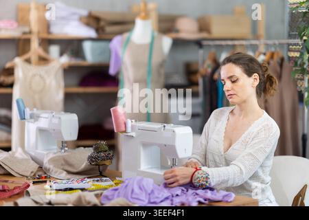 Working in sewing workshop - female dressmaker working at sewing machine making stitches on fabric Stock Photo