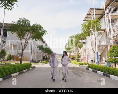 Two female industrial employees walking and talking in a modern industrial workplace environment surrounded by green landscaping and company facilitie Stock Photo