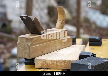 Wooden hand plane rests on a plank among sanding blocks and wood shavings on a workbench, conveying hands-on woodworking, craftsmanship and rustic wor Stock Photo