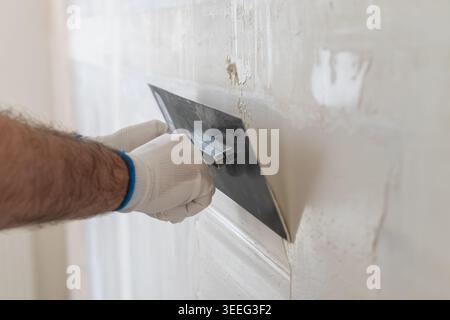 Finishing application of smooth plaster using a metal trowel on interior wall. Clean workspace with bright lighting and textured surface visible in background. Stock Photo