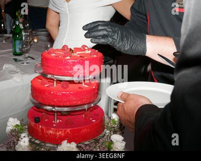 Elegant red layer cake decorated for a wedding or festive celebration, displayed on a reception table with floral accents. Stock Photo