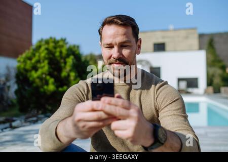 Man using smartphone in backyard and checking messages. Stock Photo