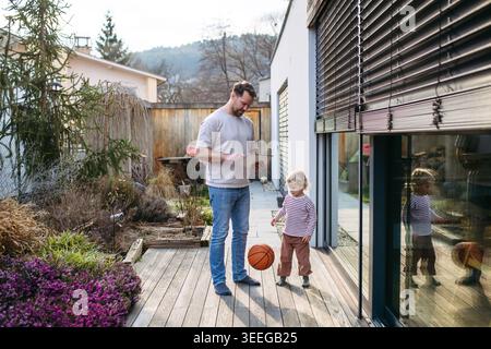 Father controlling smart home exterior blinds using tablet while standing with toddler son. Stock Photo