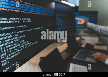 Close up of software engineer working at a multi monitor workstation with code on screens and laptop, showing software development workflow, coding pr Stock Photo