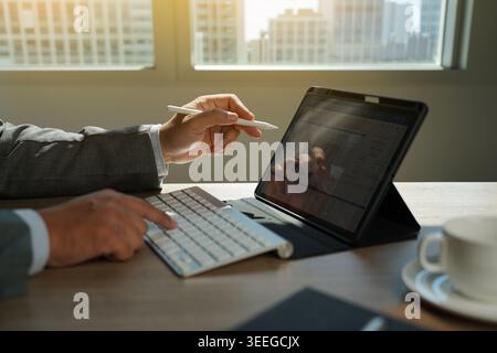 Hand using tablet with keyboard displaying financial chart data on desk, representing business analysis workflow, data reporting process, digital acco Stock Photo