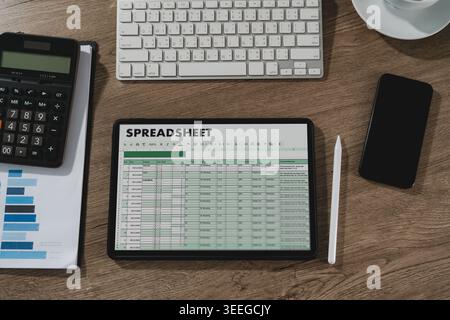 ablet displaying spreadsheet data on desk with calculator, keyboard, smartphone, and chart document, representing financial analysis workflow, account Stock Photo