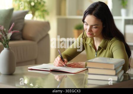 Serious young woman writing notes in paper agenda on a coffee table at home Stock Photo