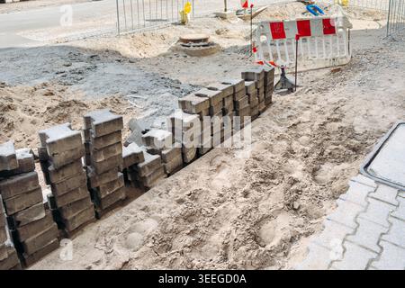 Stacks of interlocking stones sit on sand at construction site. Urban development, infrastructure improvement, city maintenance Stock Photo