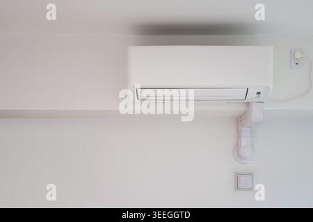 White wall-mounted air conditioning unit installed on a clean white interior wall with white conduit piping. Minimal composition ideal for real estate, home, and interior content. Stock Photo