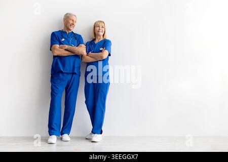 Mature medical professionals in blue scrubs standing confidently on white background Stock Photo