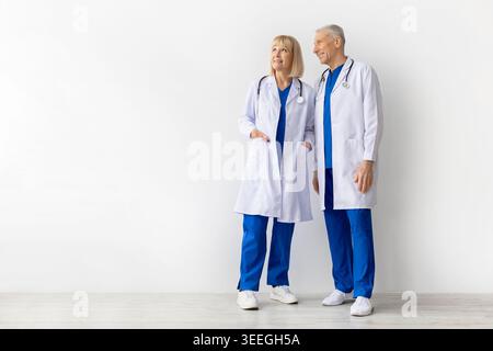 Two mature doctors in white coats and blue scrubs on white background Stock Photo
