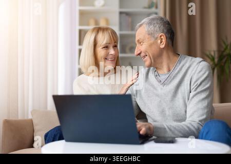 Happy mature couple using laptop together at home, smiling warmly Stock Photo