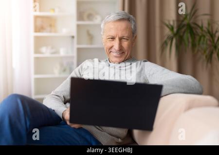 Smiling senior man relaxing at home while using laptop on sofa Stock Photo