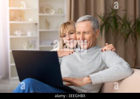 Happy mature couple using laptop together on sofa at home Stock Photo