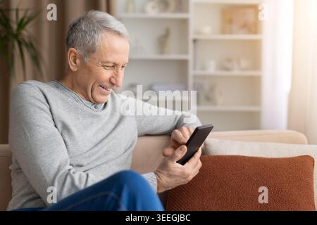 Cheerful mature man using smartphone while sitting on sofa at home Stock Photo
