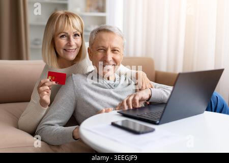 Smiling senior couple holding credit card while using laptop at home Stock Photo