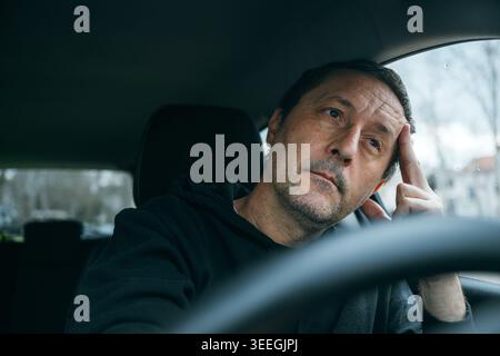 Unhappy male driver resting with hand on face inside vehicle, contemplative mood and everyday exhaustion concept, selective focus Stock Photo