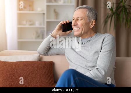 Happy senior man talking on smartphone while relaxing on sofa at home Stock Photo