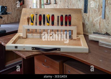 Neatly arranged chisels stored in a custom wooden rack on a shop workbench. Natural wood tones, rulers and plywood background convey craftsmanship. Stock Photo