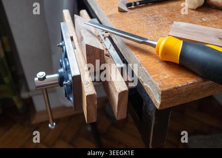 Close-up of a woodworking workbench with a chisel resting on worn wood, wooden planks held in a vise and visible signs of hands-on DIY craftsmanship. Stock Photo