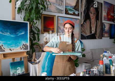 Thoughtful woman painter enjoying creative process and epoxy art, wiping dust from finished artwork. Stock Photo