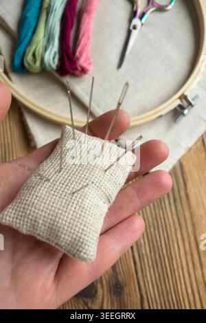 Embroidery tools and materials on wooden background: embroidery hoop with linen fabric, colorful threads, needle cushion and decorative scissors. Need Stock Photo