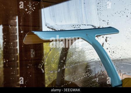 Blue window squeegee removing water and soap from wet glass surface indoors Stock Photo