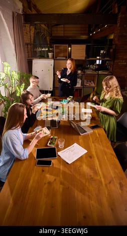Office team eating lunch together around long conference table. Stock Photo