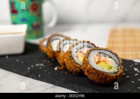 A high-angle studio shot of five pieces of homemade deep-fried sushi (tempura rolls) filled with fresh salmon and avocado. The rolls are arranged diag Stock Photo
