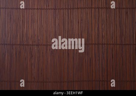 A close-up view of a woven bamboo mat, showcasing its natural texture and rich dark brown color with visible stitching Stock Photo