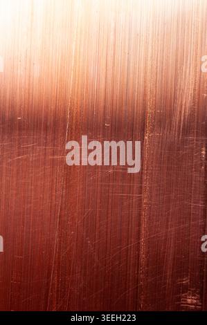 Close-up textured background of brushed copper metal showing subtle scratches and a gradient of warm light from bright to dark Stock Photo